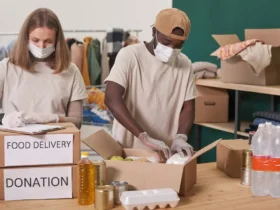 Zwei maskierte Freiwillige packen 'FOOD DELIVERY'- und 'DONATION'-Kartons mit Hilfsgütern.