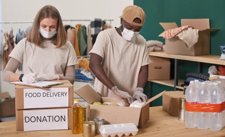 Zwei maskierte Freiwillige packen 'FOOD DELIVERY'- und 'DONATION'-Kartons mit Hilfsgütern.